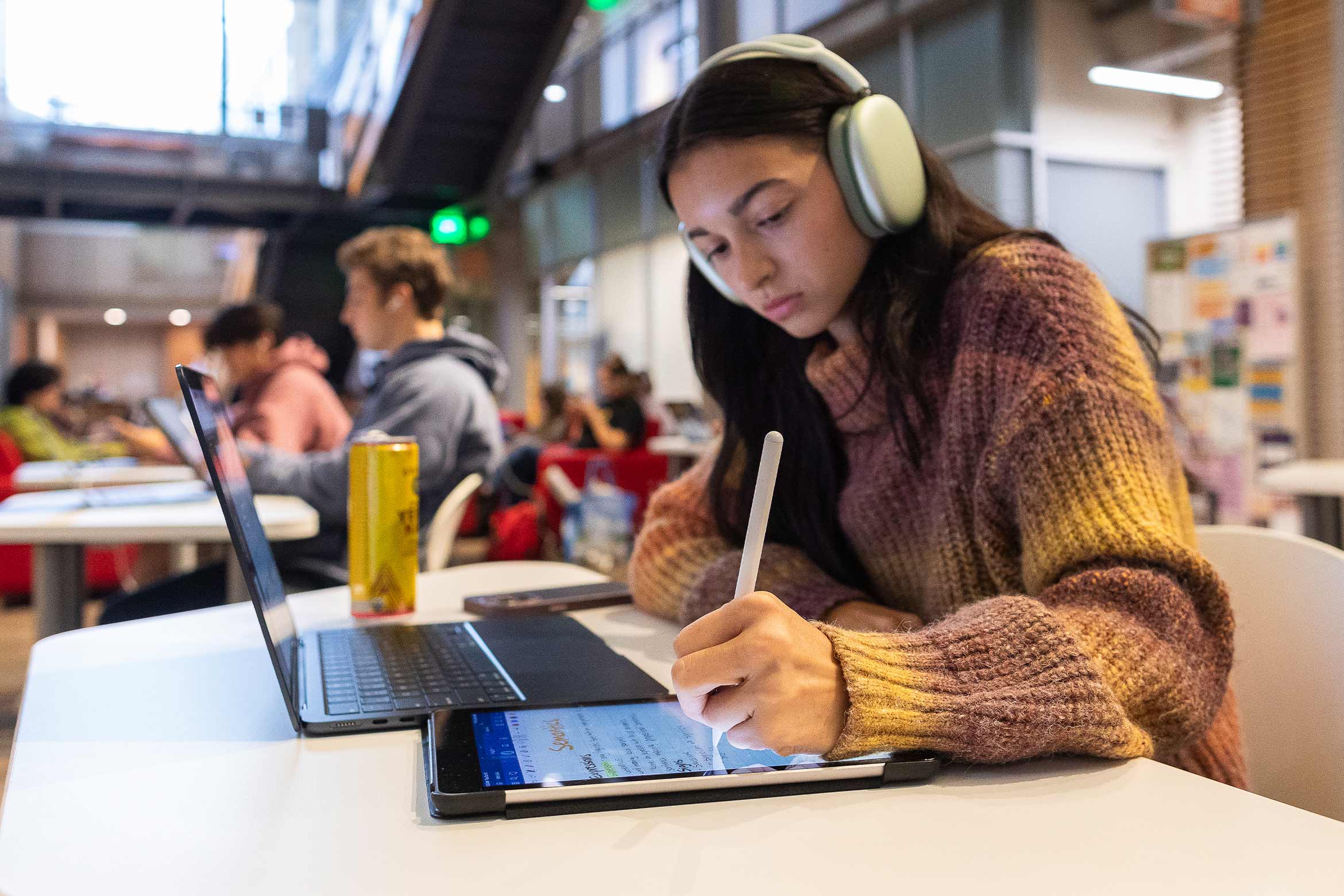 long haired person with headphones writing on a tablet.