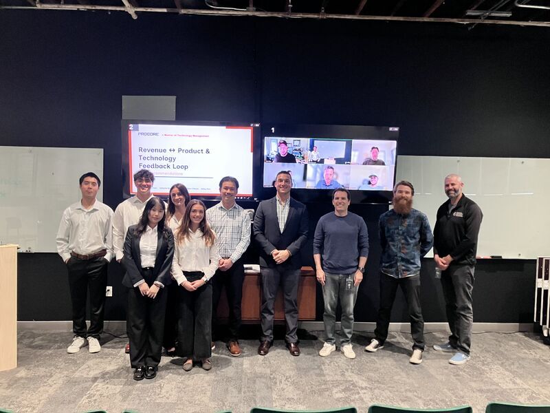 A group of MTM students and alums at the Procore offices in front of a screen with a presentation and zoom call 