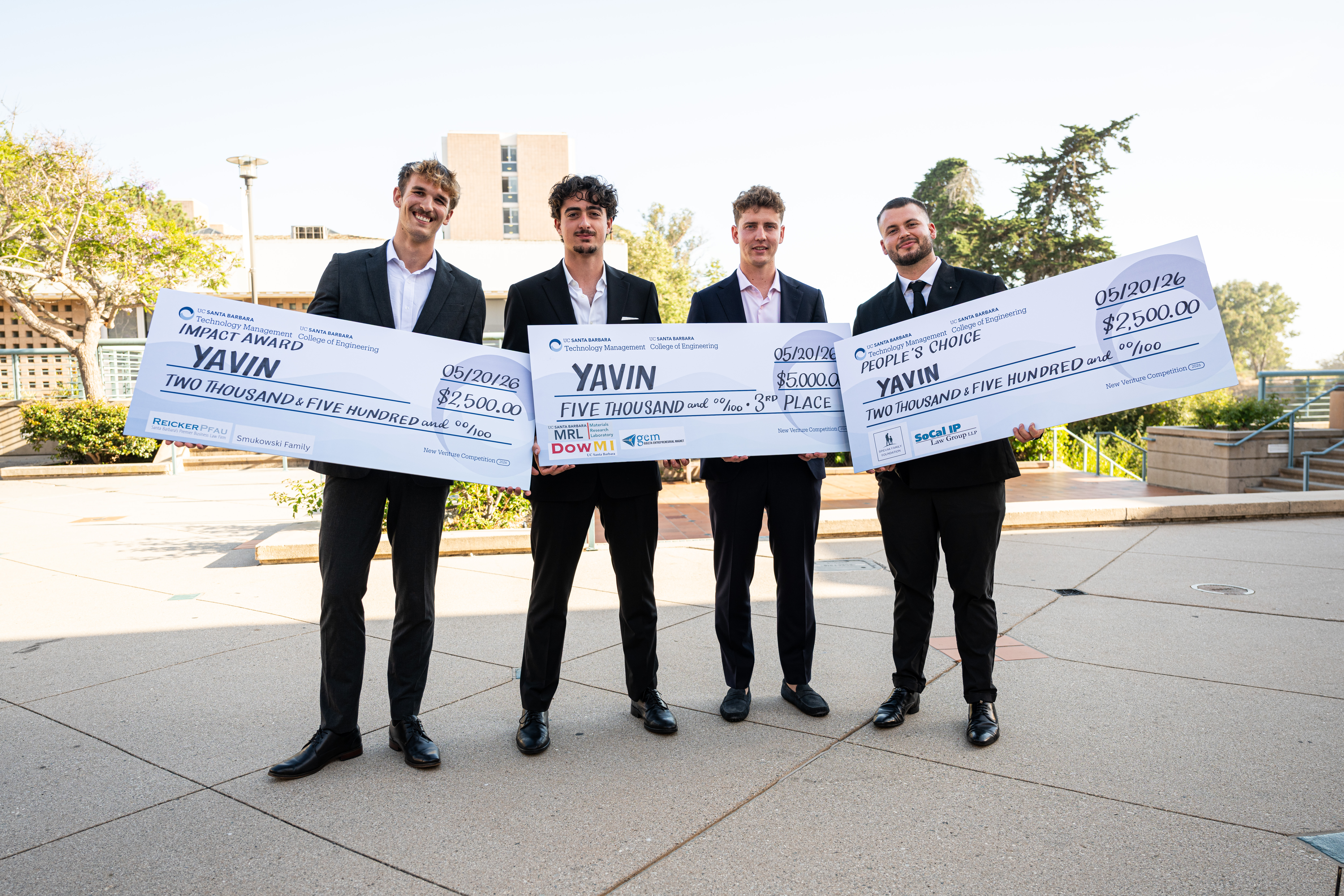 A group of students holds up three large checks