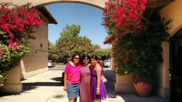 harshitha posing with her sisters in front of a decorative archway