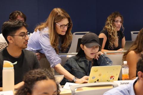 A woman in a blue shirt standing with a student at their laptop