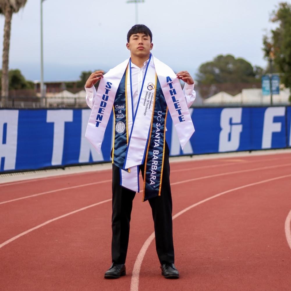 A photo of Justin Fong with graduation stolls on the UCSB track