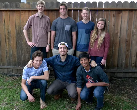 seven TMP students pose in a backyard with a wooden fence behind them