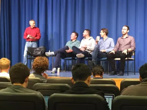 four panelists sitting on a stage with a standing presenter