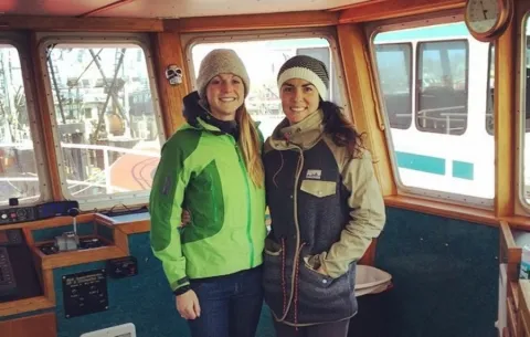 Norah Eddy and Laura Johnson bundled up in cold clothing pose inside of a boat
