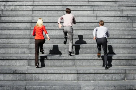 stock photo of three people running up a wide flight of concrete stairs