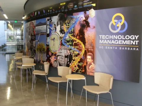 photo of what looks like a hallway in UCSB with a big TMP banner across a main curved wall and chairs and tables line the edges of the wall