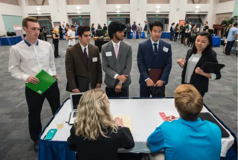 a group of TMP students gather around a company booth