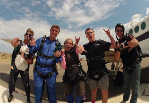 photo of Kelly with a group of guys in skydiving gear. they pose in front of a plane