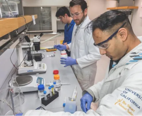 three milo sensors students work in labcoats and goggles on experiments