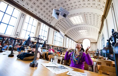 UC Berkeley's Bancroft library. A student sitting at a desk throws up her papers in excitement