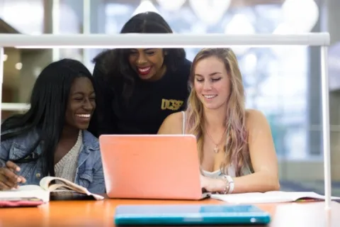stock photo of three girls looking at something on an orange laptop
