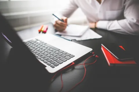 businessperson writing notes on a notebook while looking at his macbook