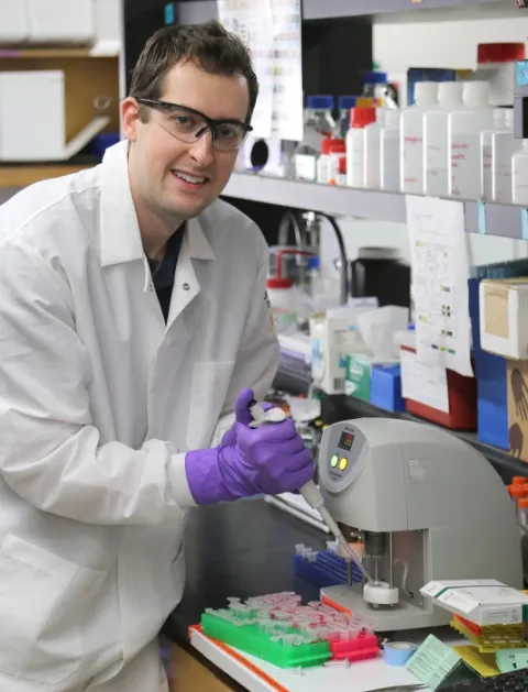 Damien Kudela posing with an experiment he's holding under a microscope