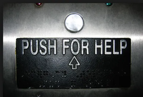 a closeup of the inside of an elevator button with a sign beneath it that reads "push for help"